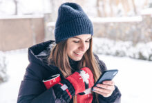 happy young woman in mittens with a cup looks at the phone screen