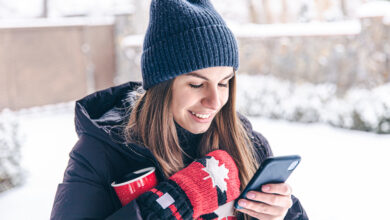 happy young woman in mittens with a cup looks at the phone screen