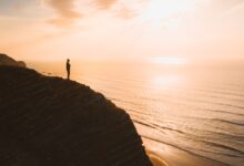 beautiful view of a person standing on a cliff over the ocean at sunset in algarve portugal