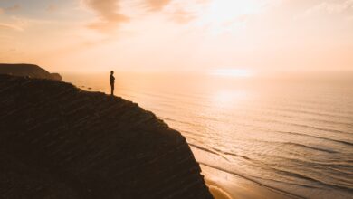 beautiful view of a person standing on a cliff over the ocean at sunset in algarve portugal